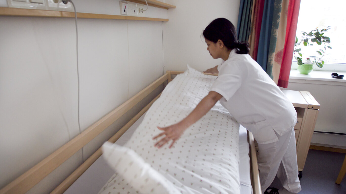 Bildet viser en helsefagarbeider som rer opp en seng.