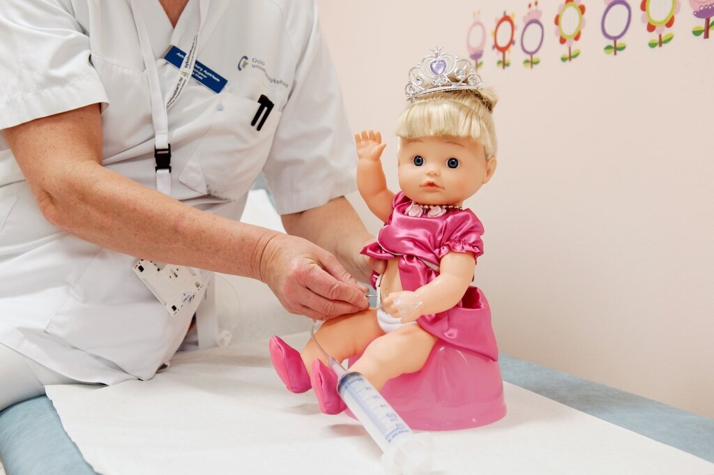 Stomi, demonstrasjon Bildet viser en dukke som sitter på rosa potte og har åpning på magen som brukes til å skylle tarmen.