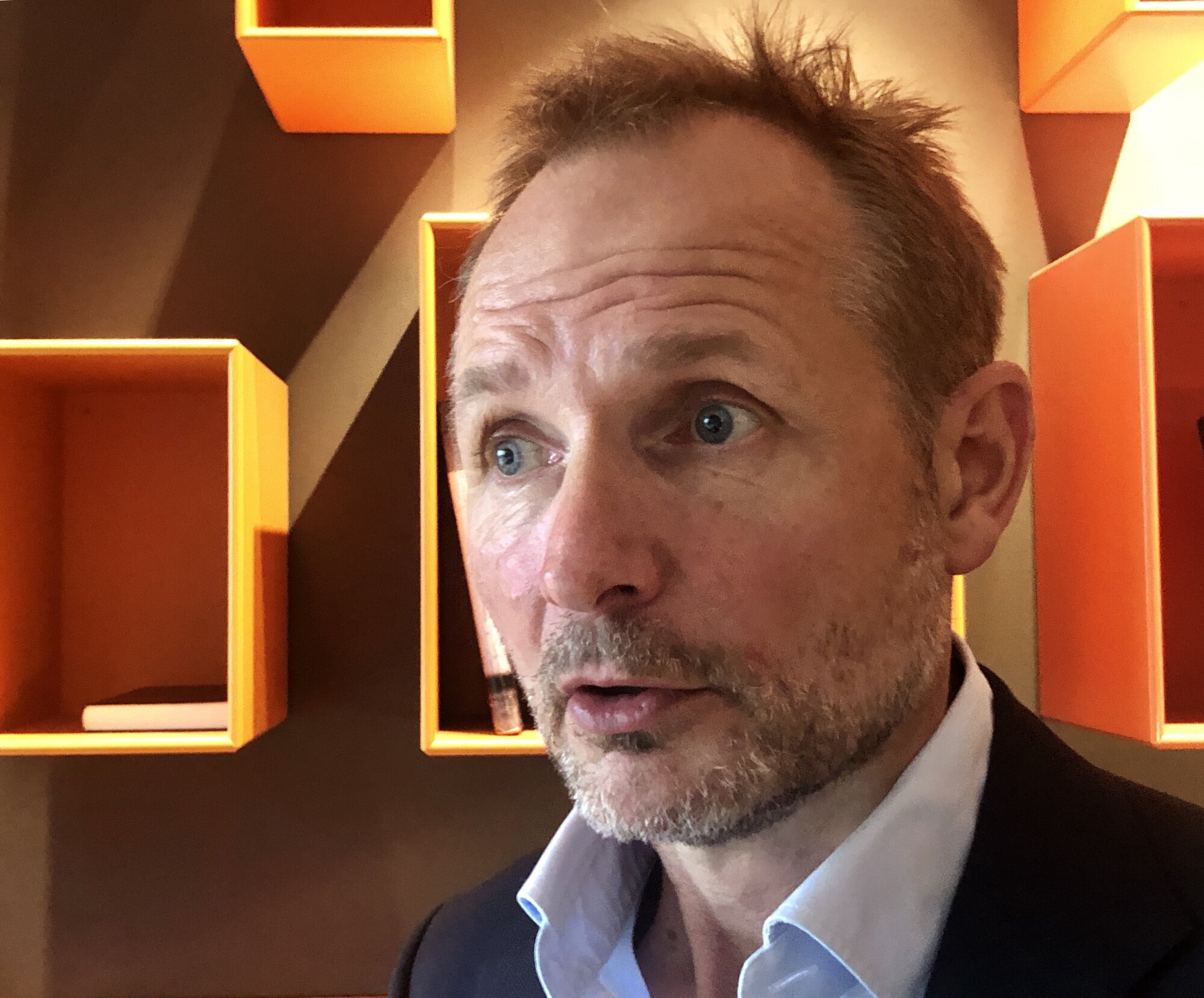 Engasjert mann, portrett foran vedd med kubeformede oransje bokhyller.