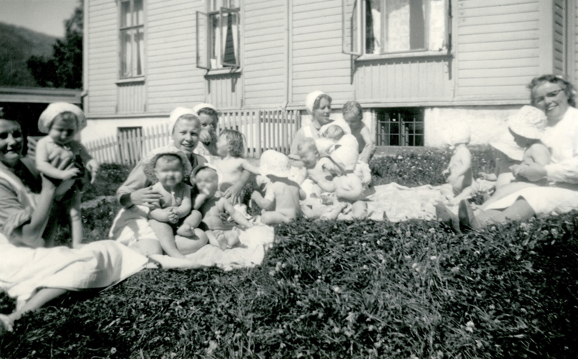 Historisk, gammelt bilde av sykepleiere med små barn på gresset utenfor Bergen kommunale mødrehjem. Historisk, gammelt bilde av sykepleiere med små barn på gresset utenfor Bergen kommunale mødrehjem.