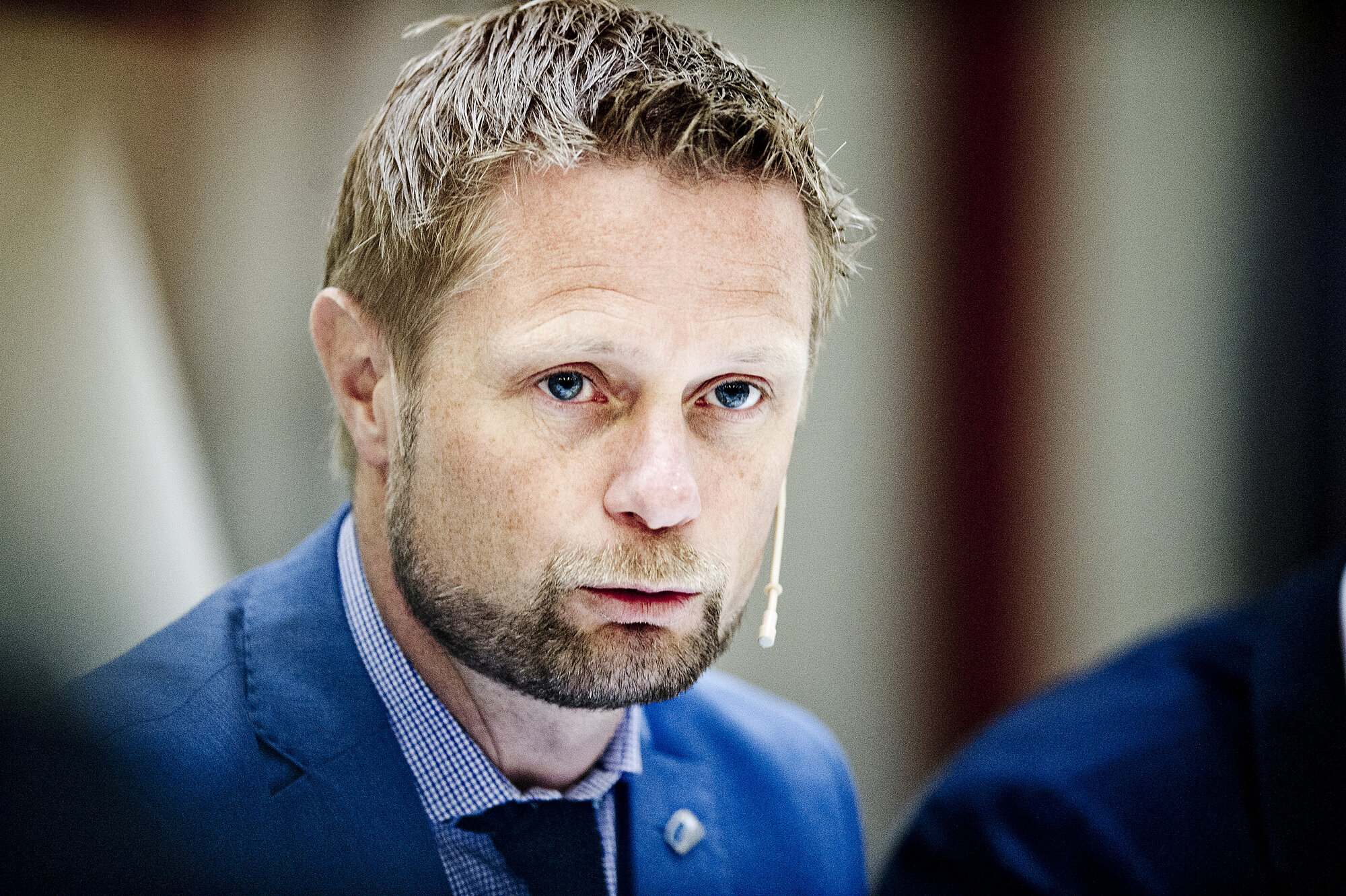 Portrett av Bent Høie med kikrofon og blå dress, lener seg mot bordet