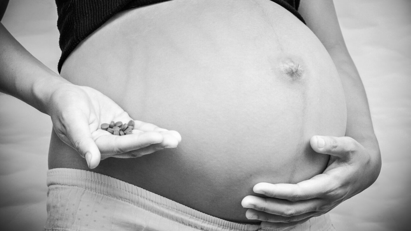 Bildet viser en gravid mage og en hånd som holder mange piller.