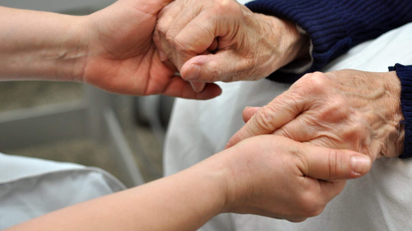 Bildet viser hendene til en sykepleier som holder hendene til en eldre person.
