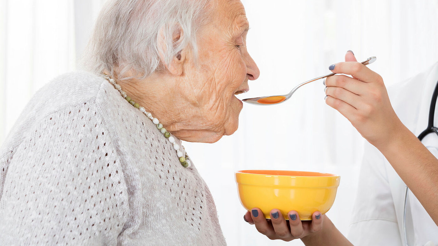 Bildet viser en eldre kvinne som blir matet av en sykepleier.