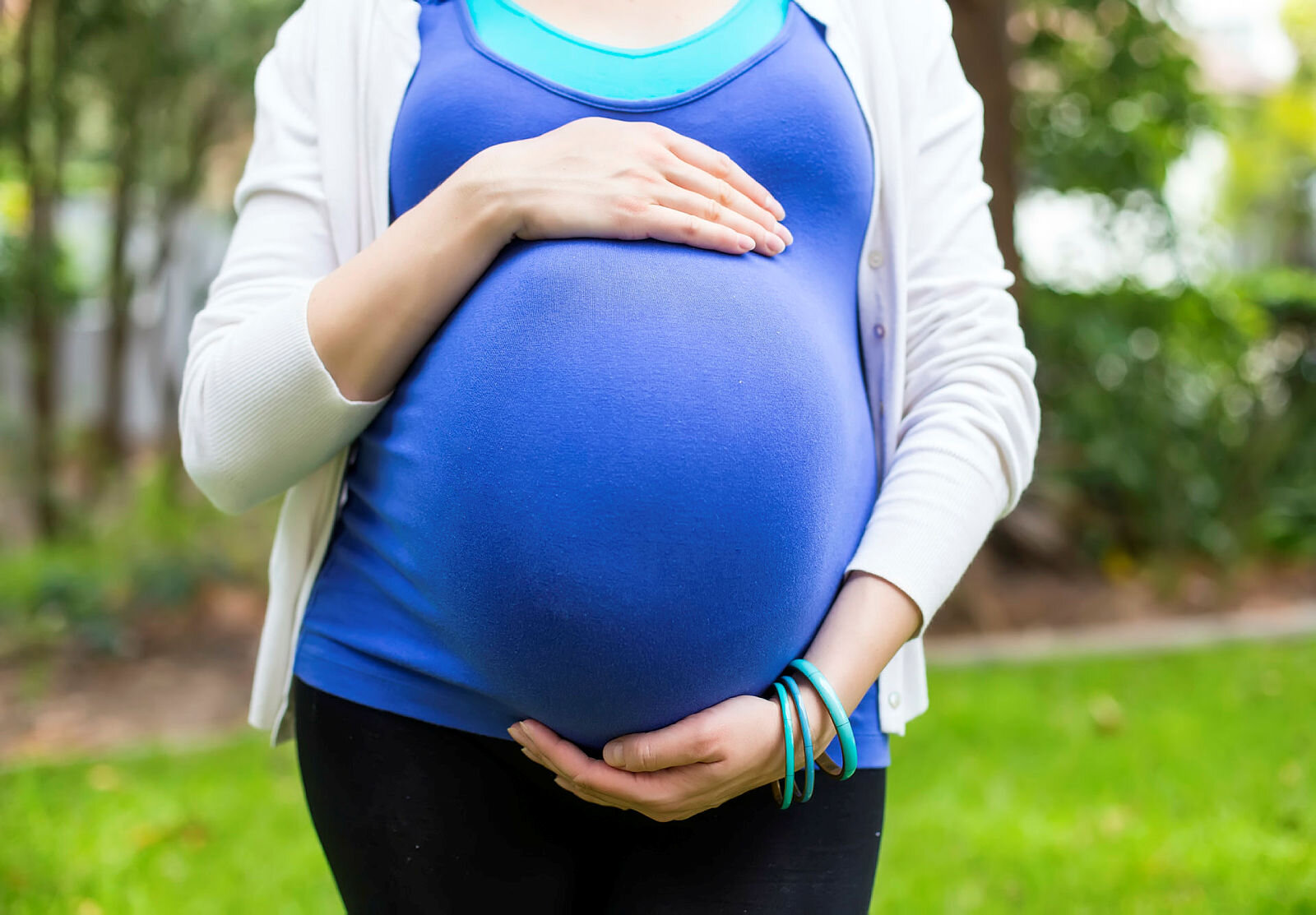 Gravid kvinne Bildet viser en gravid kvinne med blå topp som holder rundt magen sin