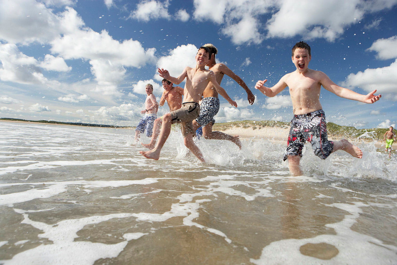 Bading Bildet viser en gjeng med gutter som løper ut i vannet på en strand