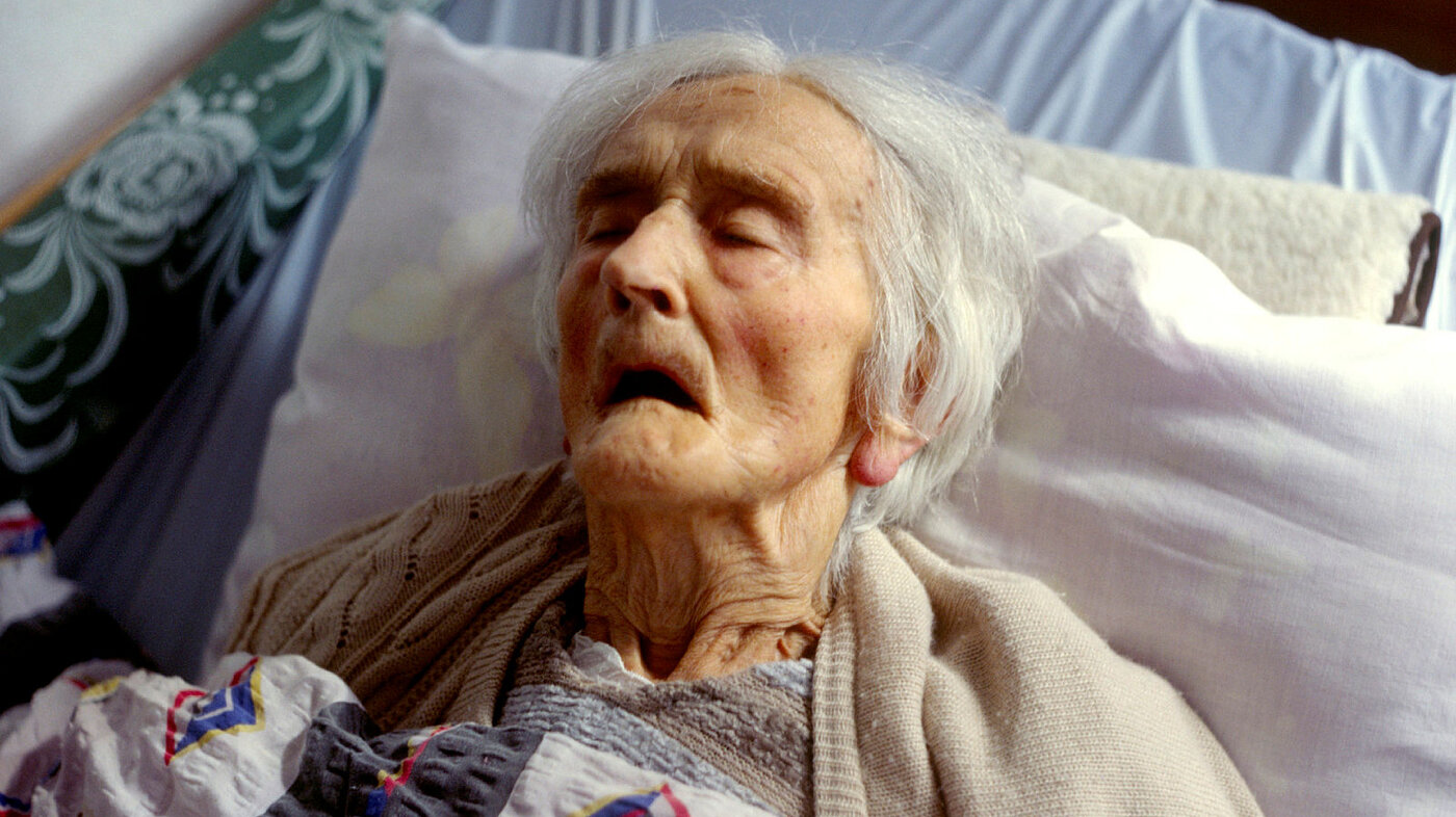 Bildet viser en eldre kvinne som ligger død i en seng