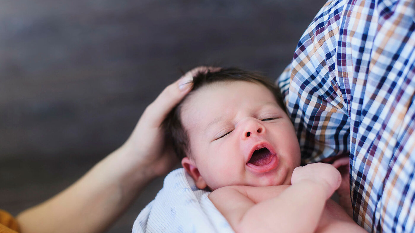 Baby Liten baby som gjesper mens han/hun får kos av mor og far.
