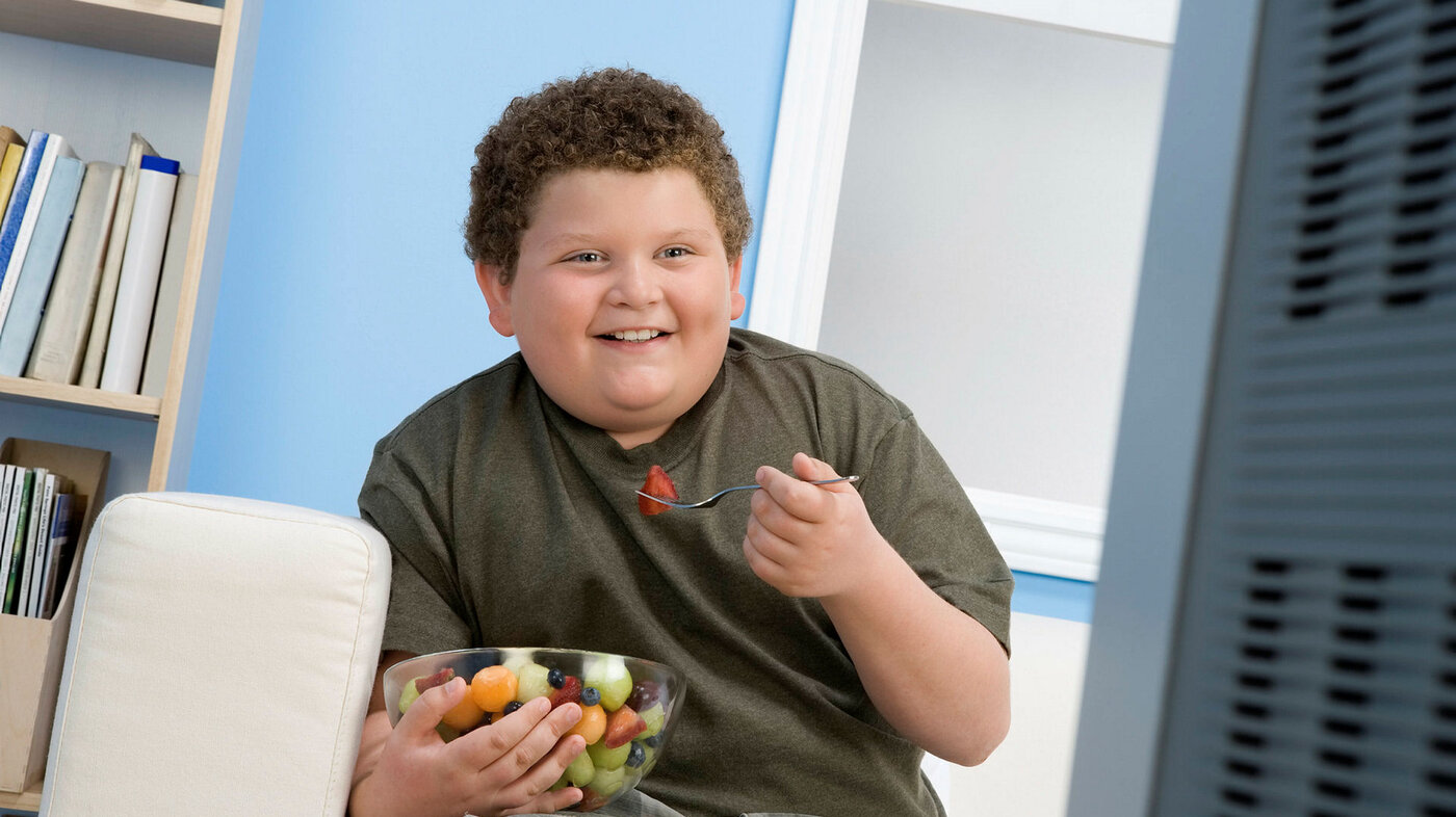 Bildet viser en overvektig gutt som sitter i en stol og spiser druer.