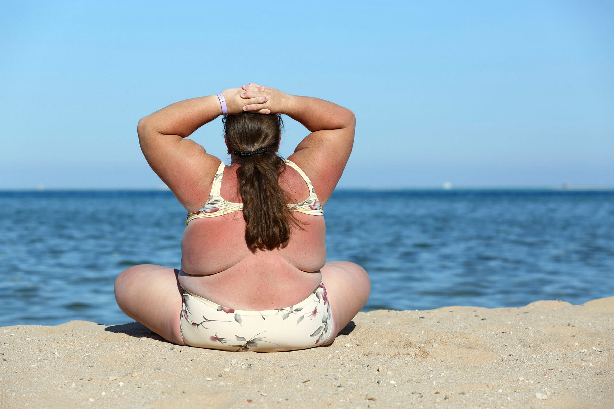 Kvinne på stranden Bildet viser en overvektig kvinne bakfra, som sitter på stranden i bikini.