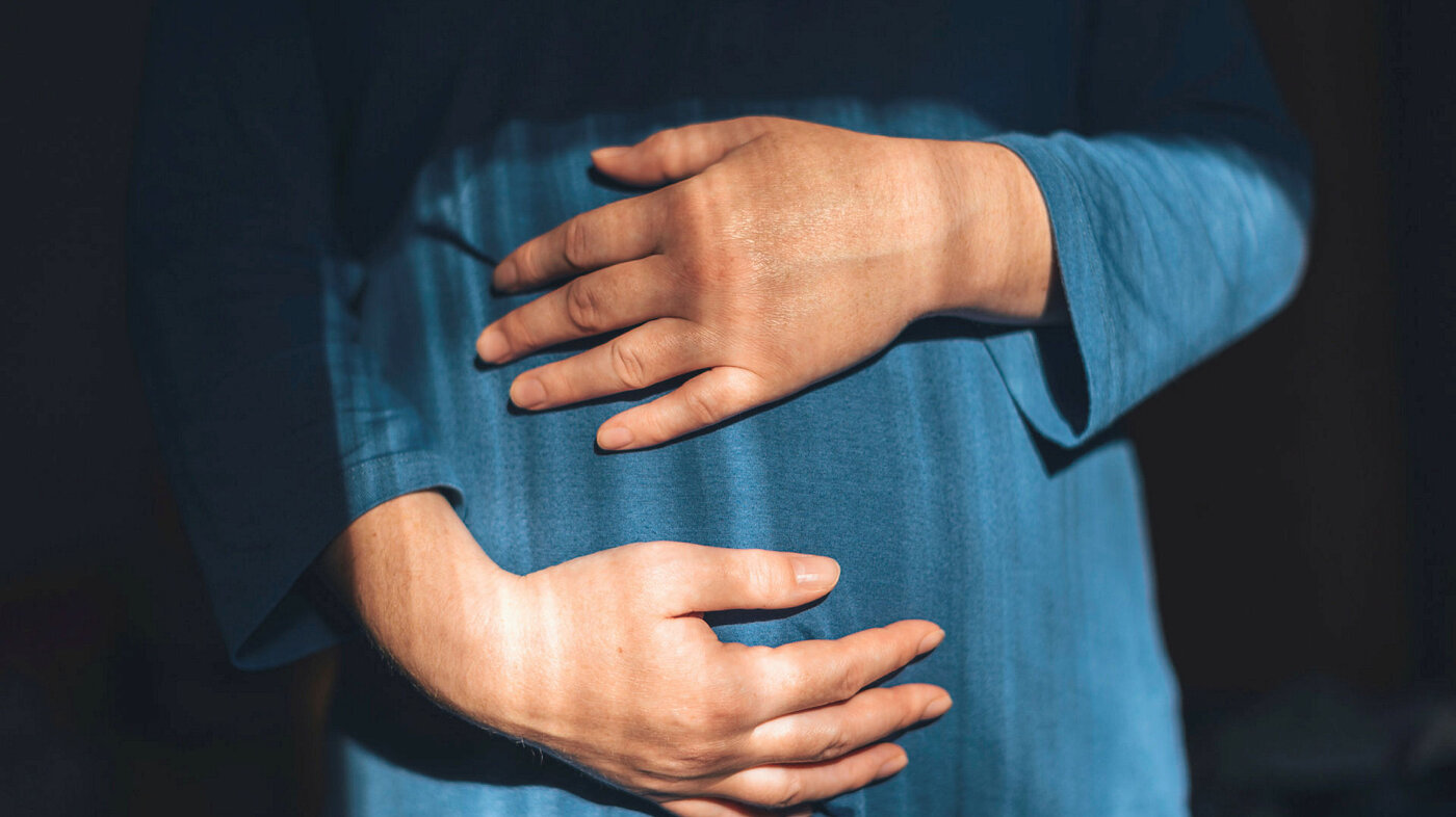 Gravid kvinne med hendene rundt magen.