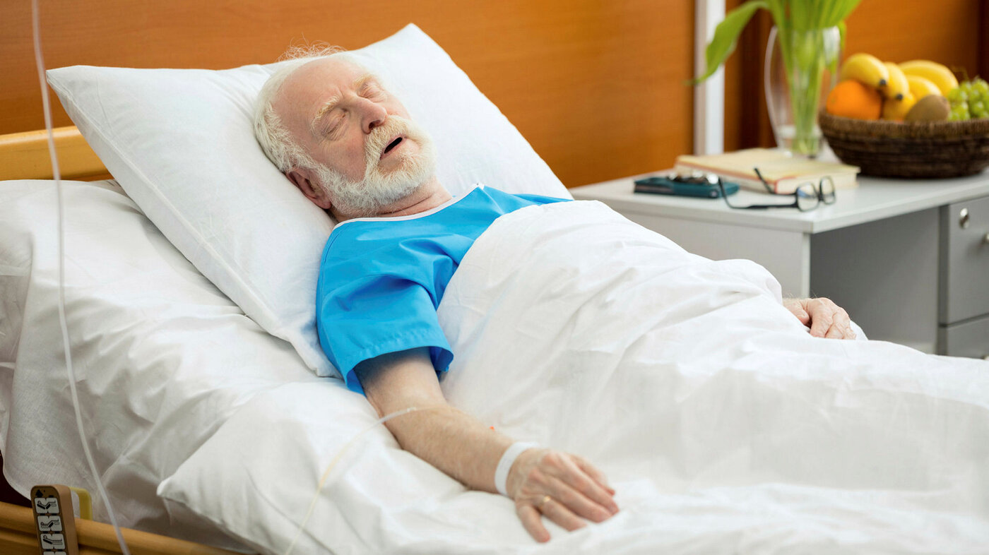 Bildet viser en eldre, syk mann i sengen på sykehus.