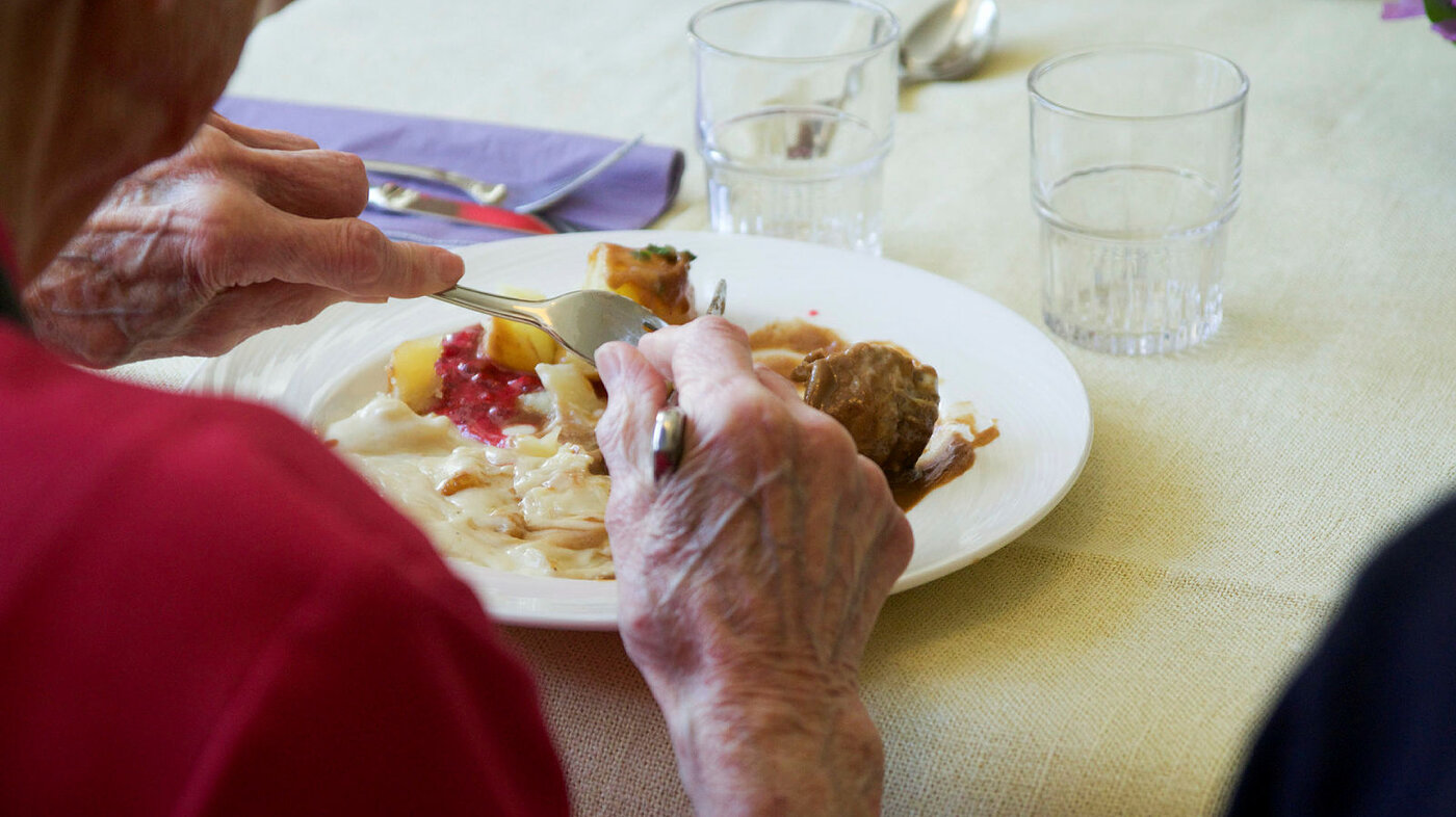 Bildet viser en eldre mann eller kvinne som spiser middag