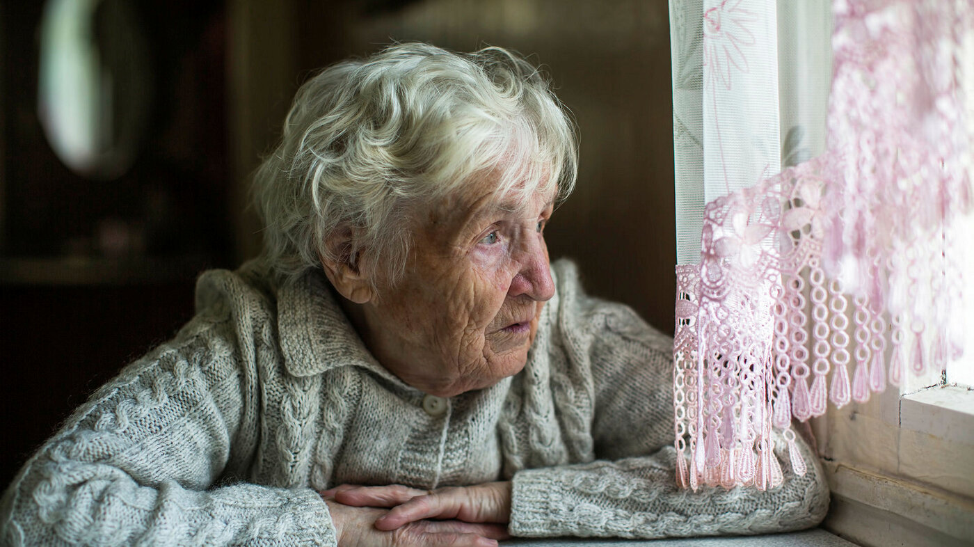 Bildet viser en eldre kvinne som ser ut av vinduet