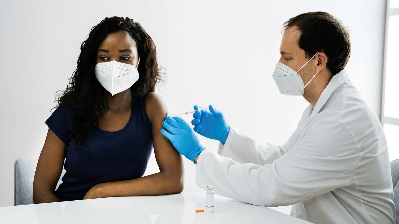 Bildet viser en kvinne med munnbind som blir vaksinert av et helsepersonell med munnbind