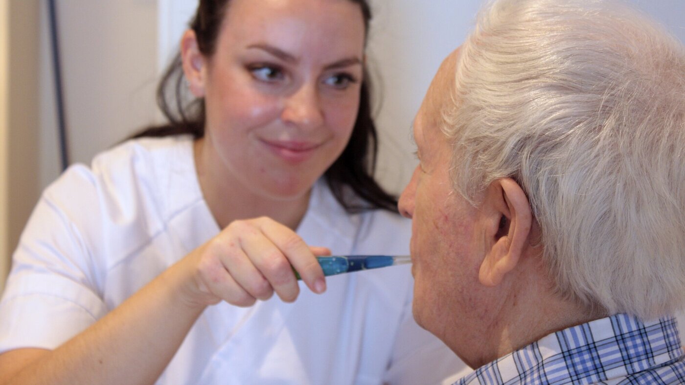 Bildet viser en sykepleier som pusser tennene til en eldre mann