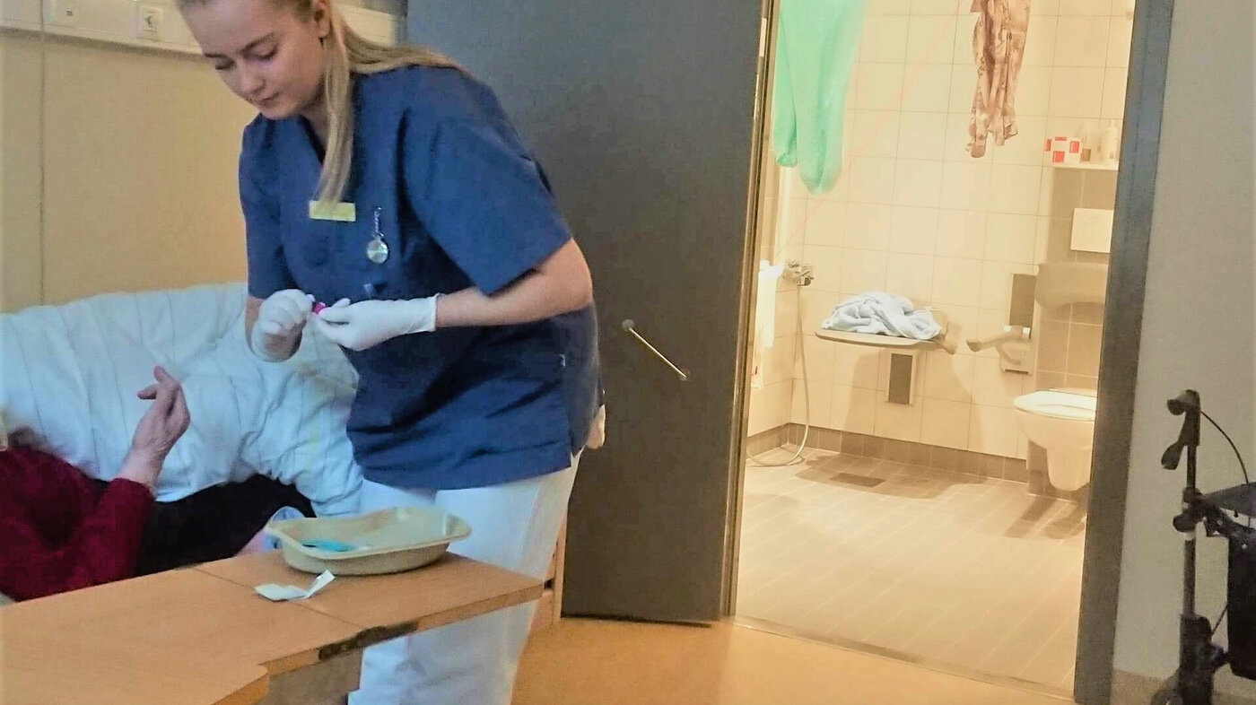 Bildet viser sykepleierstudent Stine Sundberg som har praksisplass på et eldrehjem. Hun hjelper en sengeliggende beboer.