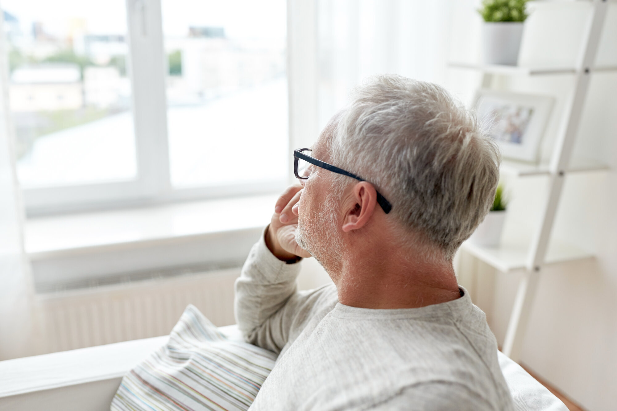 Lyst kledd middelaldrende mann sitter og ser ut av vindu. Hvitt lys.