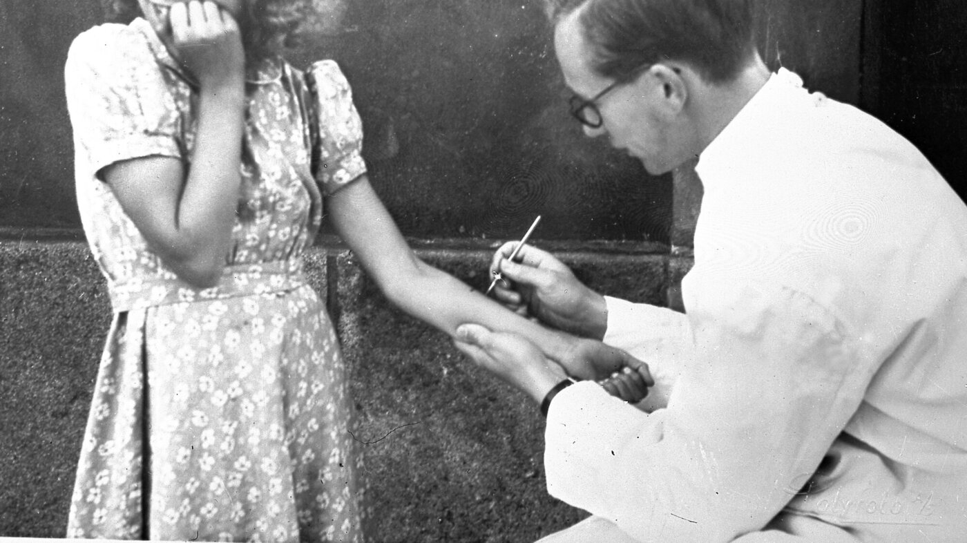 Bildet viser en jente som ser bort, med et lite angsfylt smil rundt munnen, mens en lege tar tuberkulintest.