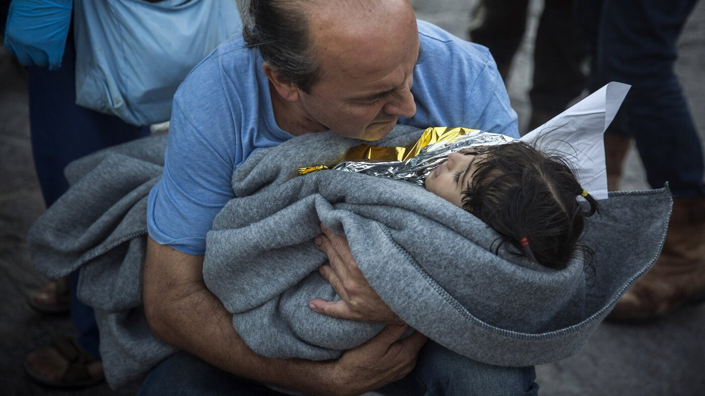 Bildet viser en mann med et lite barn inntullet i teppe i armene.