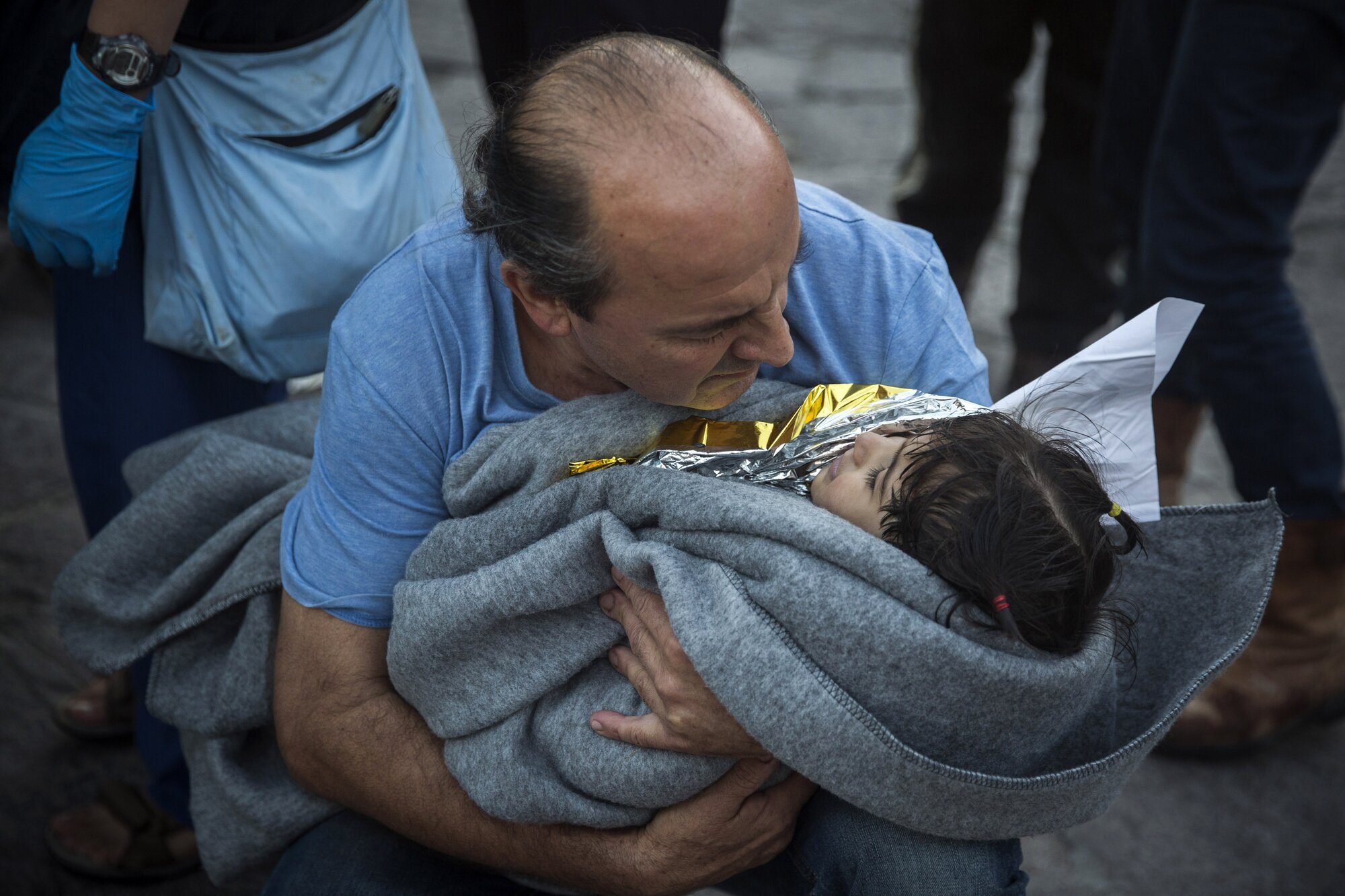 flyktninger, Lesbos Bildet viser en mann med et lite barn inntullet i teppe i armene.