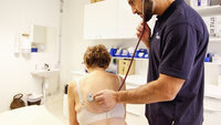 Bildet viser en lege som lytter på ryggen til en kvinnelig pasient.