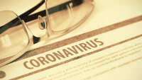 Bildet viser et par briller som ligger over en papirartikkel med overskrift Coronavirus.