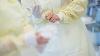 Bildet viser sykepleiere i gult smittevernutstyr som tar på seg hansker.