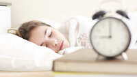 Tenåring som sover med en vekkeklokke i forgrunnen