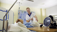 Bildet viser en sykepleierstudent som står ved siden av en seng hvor det ligger en simuleringsdukke