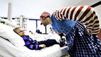 Bildet viser en av Sykehusklovnenes klovner sammen med et barn som ligger i en sykehusseng