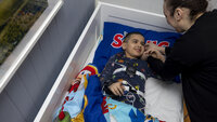 The photo shows a boy lying in his bed. Tools for sleep testing and monitoring are equipped on the boy. His mother is bending towards him, both are smiling