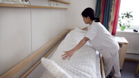 Bildet viser en helsefagarbeider som rer opp en seng.