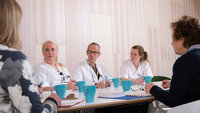Bildet viser helsepersonell som sitter rundt et bord. Noen har uniform, andre ikke.
