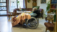 Bildet viser en eldre kvinne liggende i en rullestol i en stue på et behandlingssenter.  