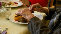 Bildet viser et middagsbord på sykehjem med to middagstallerkner og hender til to gamle personer