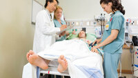 Bildet viser en pasient som ligger i en sykehusseng mens to sykepleiere og en lege står ved siden av. Legen skriver på et skjema.