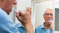 Bildet viser en eldre mann foran et speil som pusser tennene.