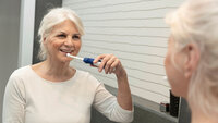 Bildet viser en eldre kvinne som pusser tennene med en elektrisk tannbørste