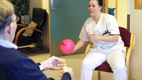 Bildet viser sykepleier Kine-Marita Krüger på Sentrum sykehjem, Bodø som kaster en ball til en eldre pasient som sitter med ryggen til.