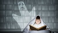 En ung gutt sitter i senga og leser skummel bok